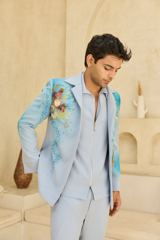 Man wearing a light blue suit with floral embroidery in an indoor setting